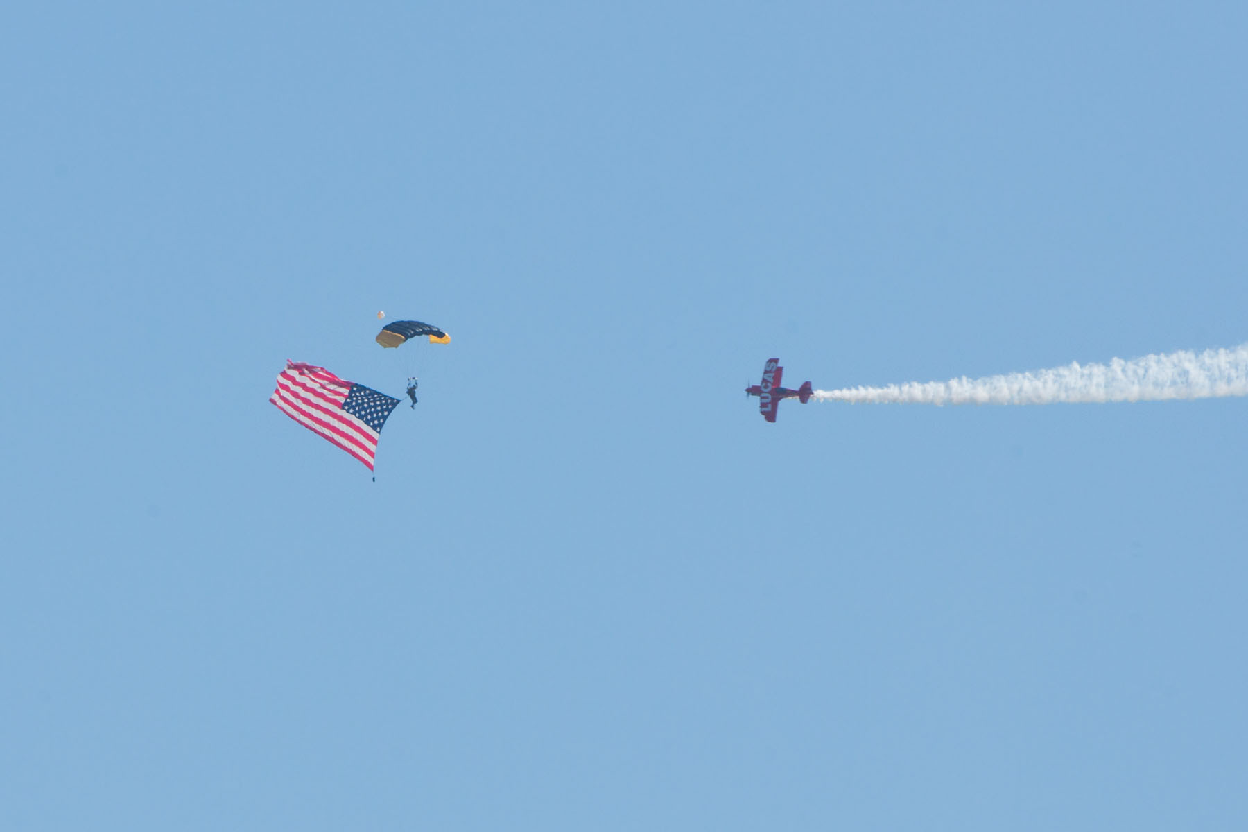 Skydiver brings in the flag, Sioux Falls Air Show, August 2019.  Lucas Oil stunt plane escorts him down.  Click for next photo.